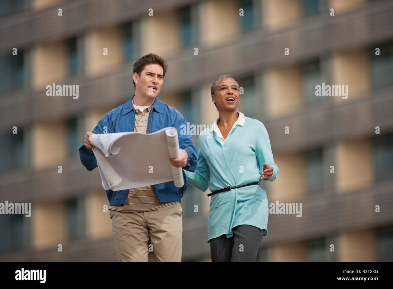 Two young engineers discussing building plans at a construction site. Stock Photo