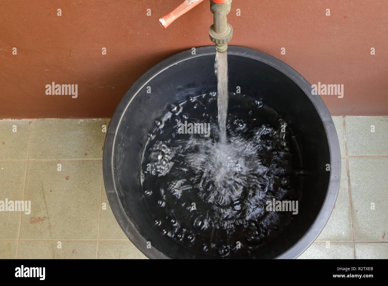 top view of water flowing into a big black bucket on dirty floor, saving concept Stock Photo