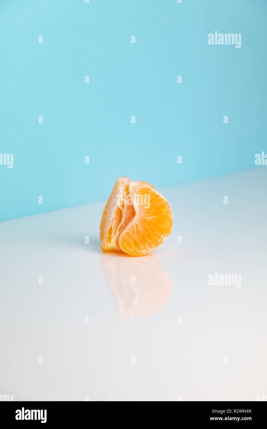 Wedges of tangerine on white table. Minimalistic image of piece of orange fruit on bright studio background Stock Photo