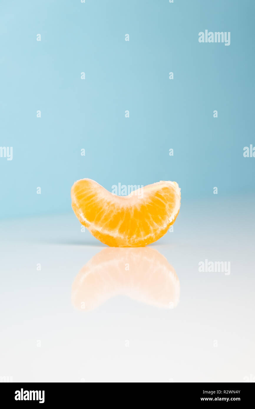 Wedge of tangerine on white and blue background. Minimalistic image of piece of orange fruit at sparse bright environment. Stock Photo