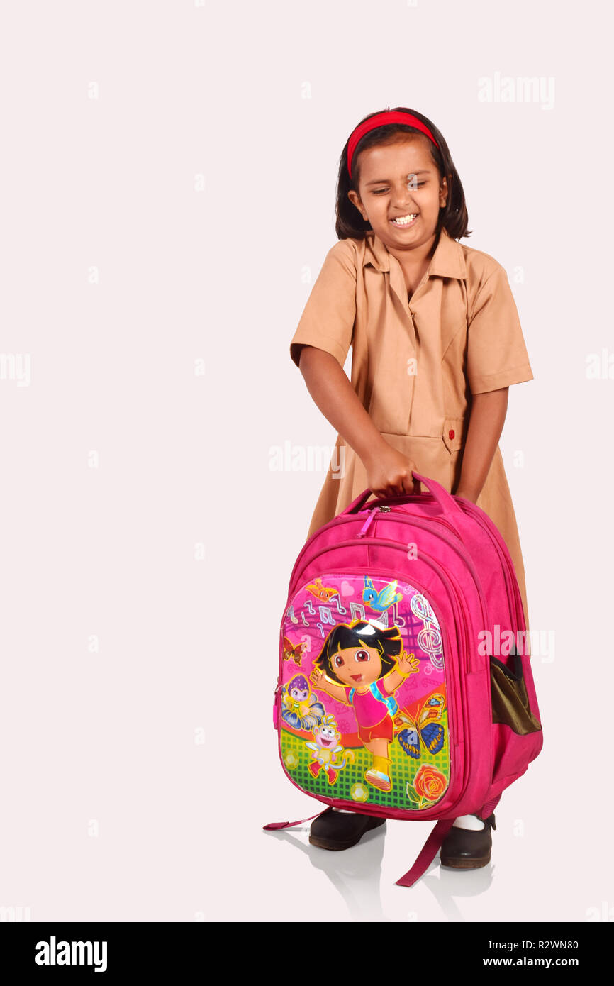 Little girl in school uniform picking a heavy school bag. Pune