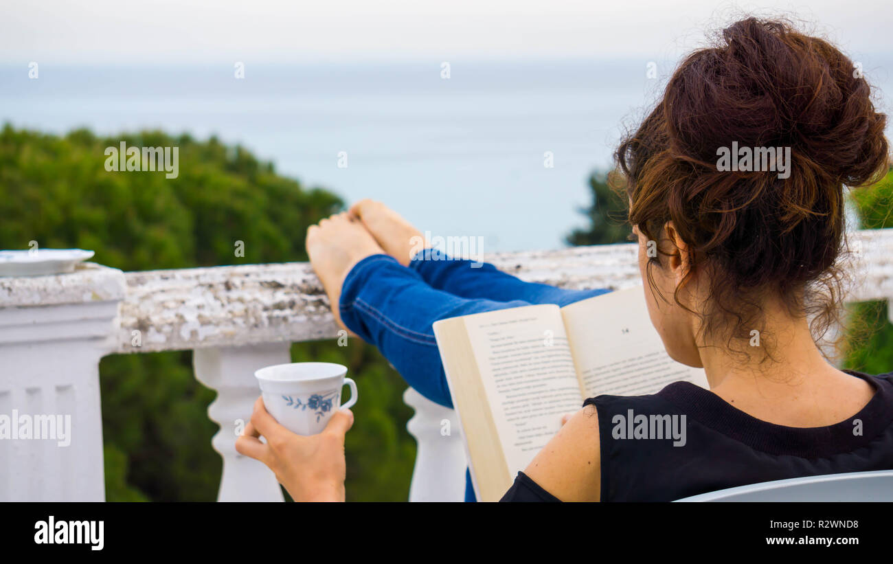 Pretty relaxed young woman reading a book at the balcony Stock Photo ...