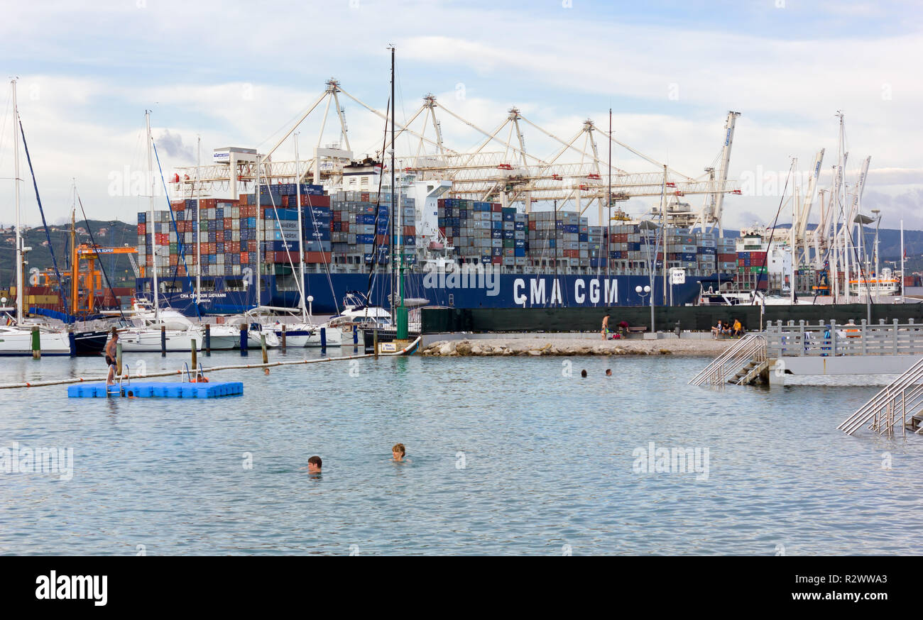 KOPER, Slovenia - July 24, 2014: a few bathers in the waters before the seaport, with a big container ship in the background Stock Photo