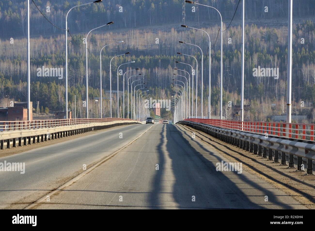 Perspective view on tarmac road on river bridge with lamp posts in Siberia, Russia Stock Photo