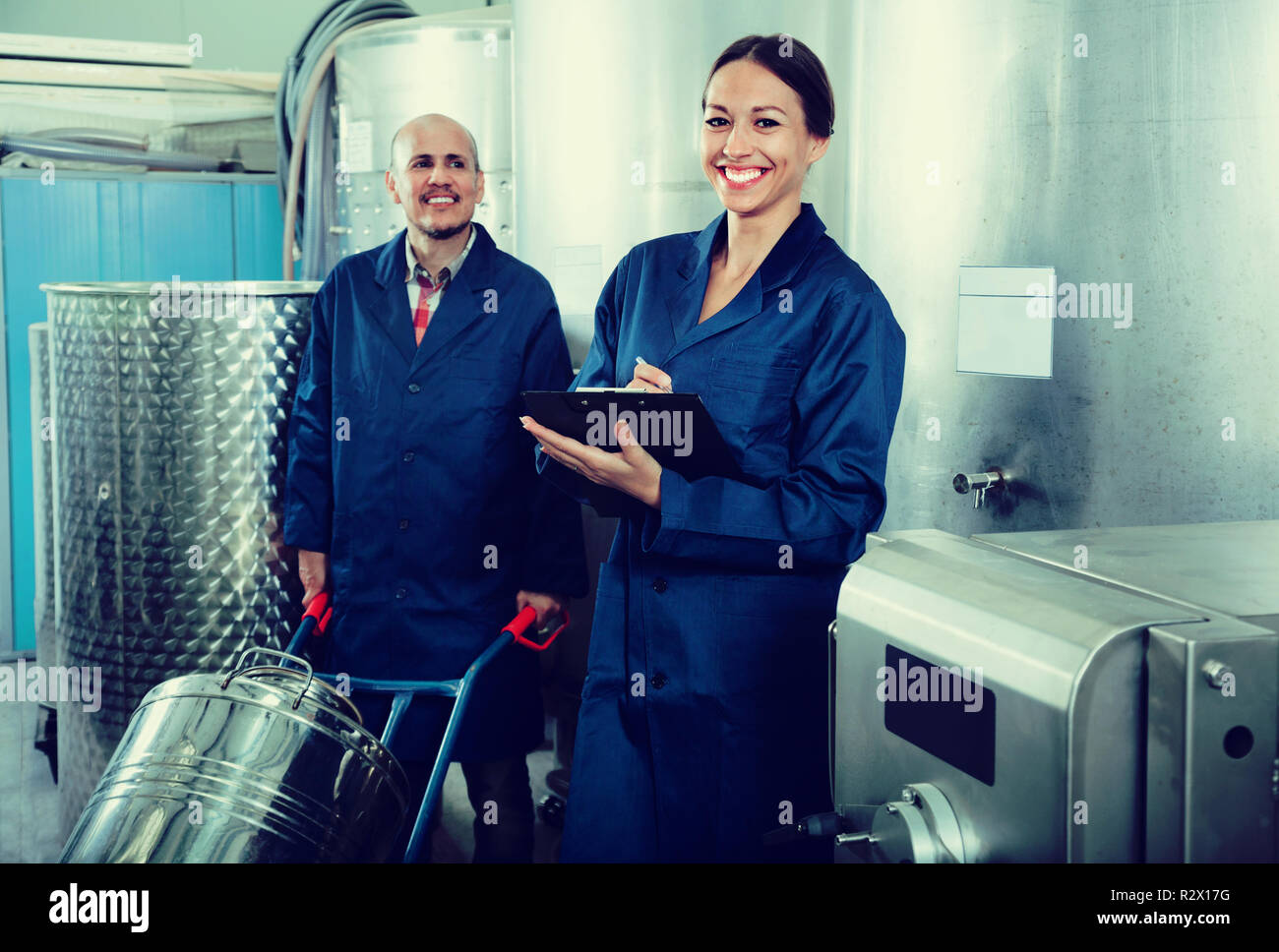 Glad diligent positive female winery worker taking notes while male one working in fermentation section Stock Photo