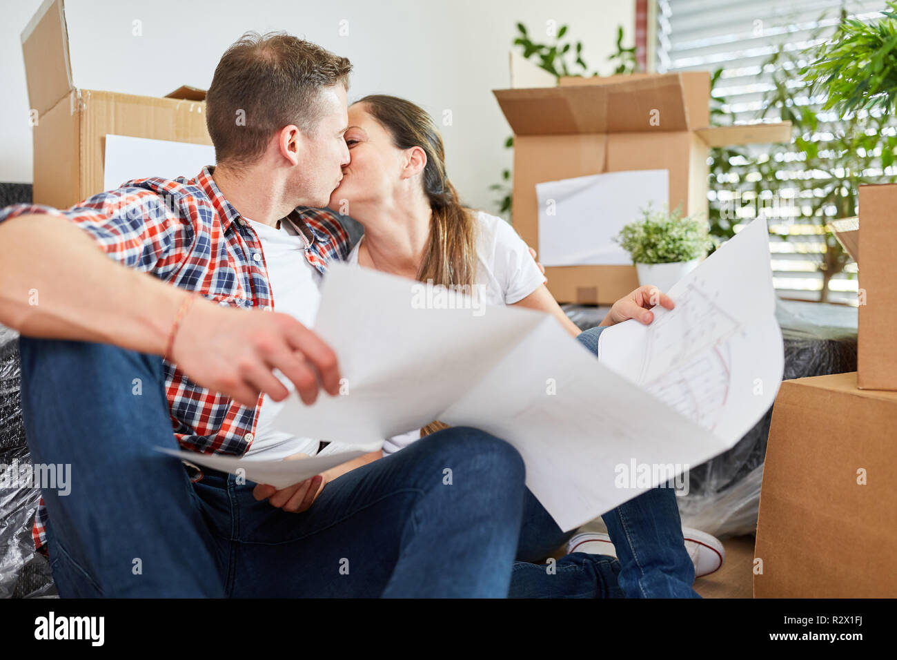 Young couple with blueprint kissing in love and looking forward to their new home Stock Photo