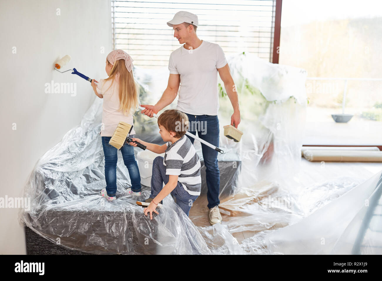 Children paint wall together with father while renovating before moving ...