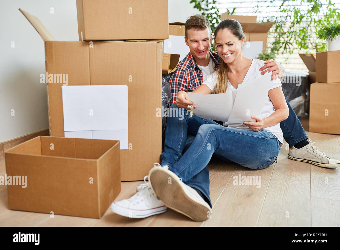 Young happy couple is sitting in the new apartment between moving boxes Stock Photo
