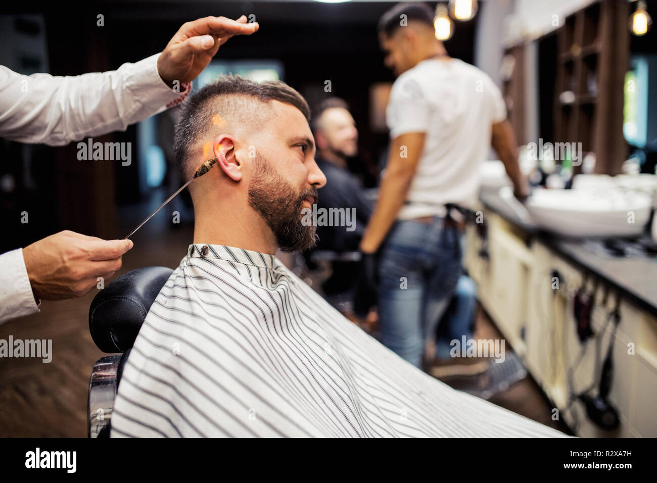 Hipster man client visiting haidresser and hairstylist in barber shop, ear  hair removal Stock Photo - Alamy