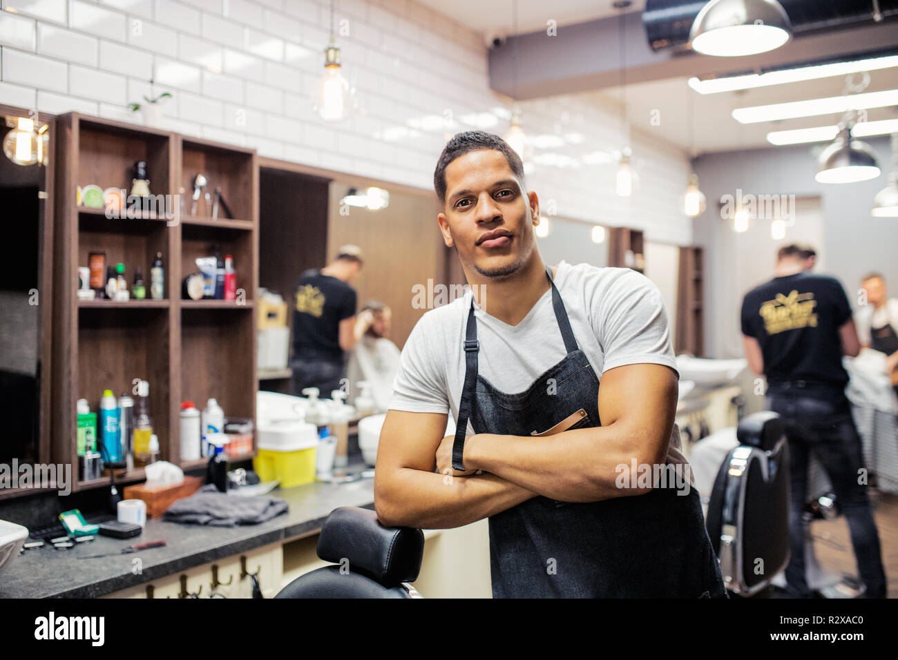 Young hispanic haidresser and hairstylist standing in barber shop, arms crossed. Stock Photo