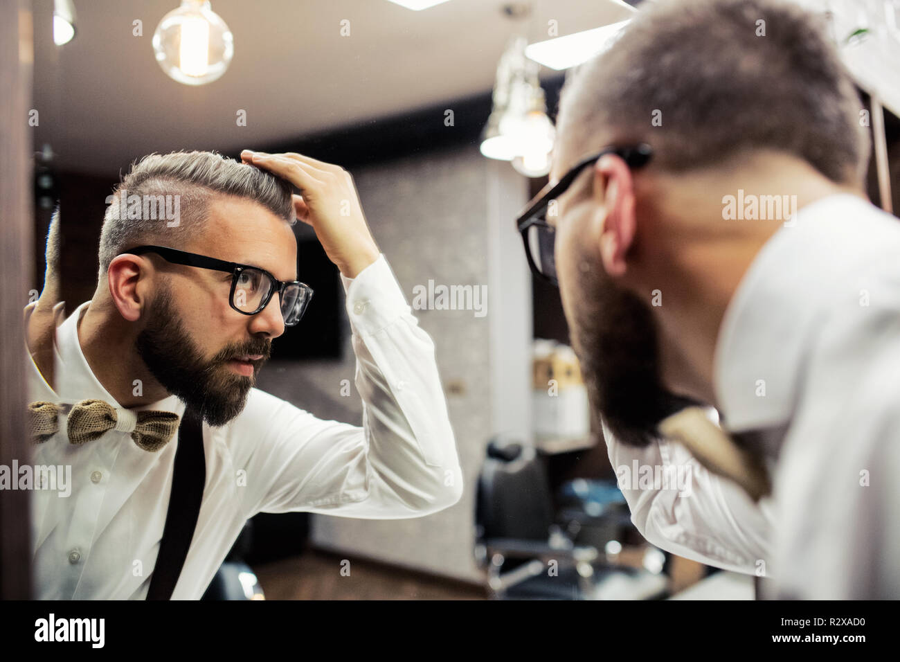 Hipster man client with glasses looking in the mirror in barber shop. Stock Photo