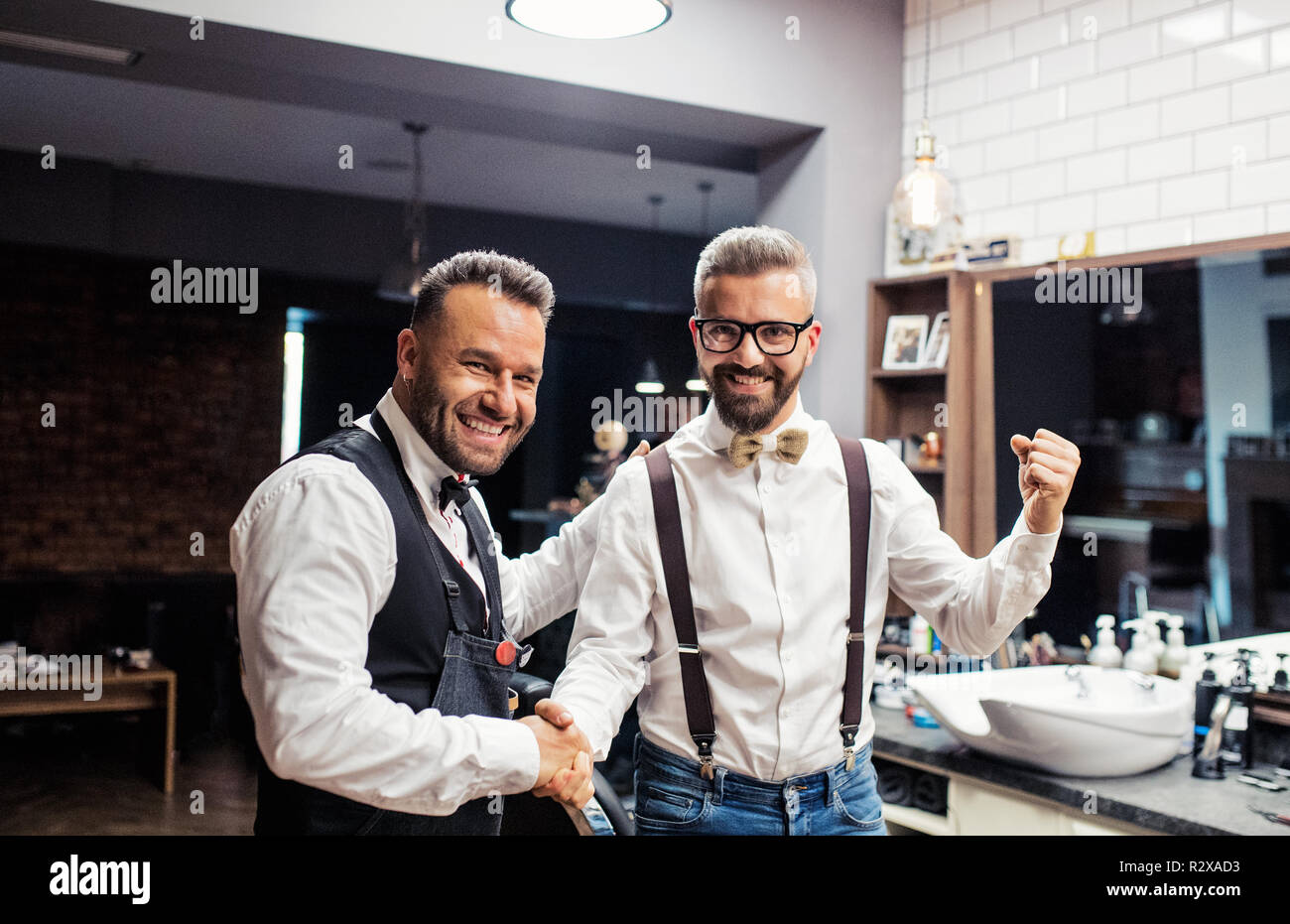 Hipster man client shaking hands with haidresser and hairstylist in barber shop. Stock Photo