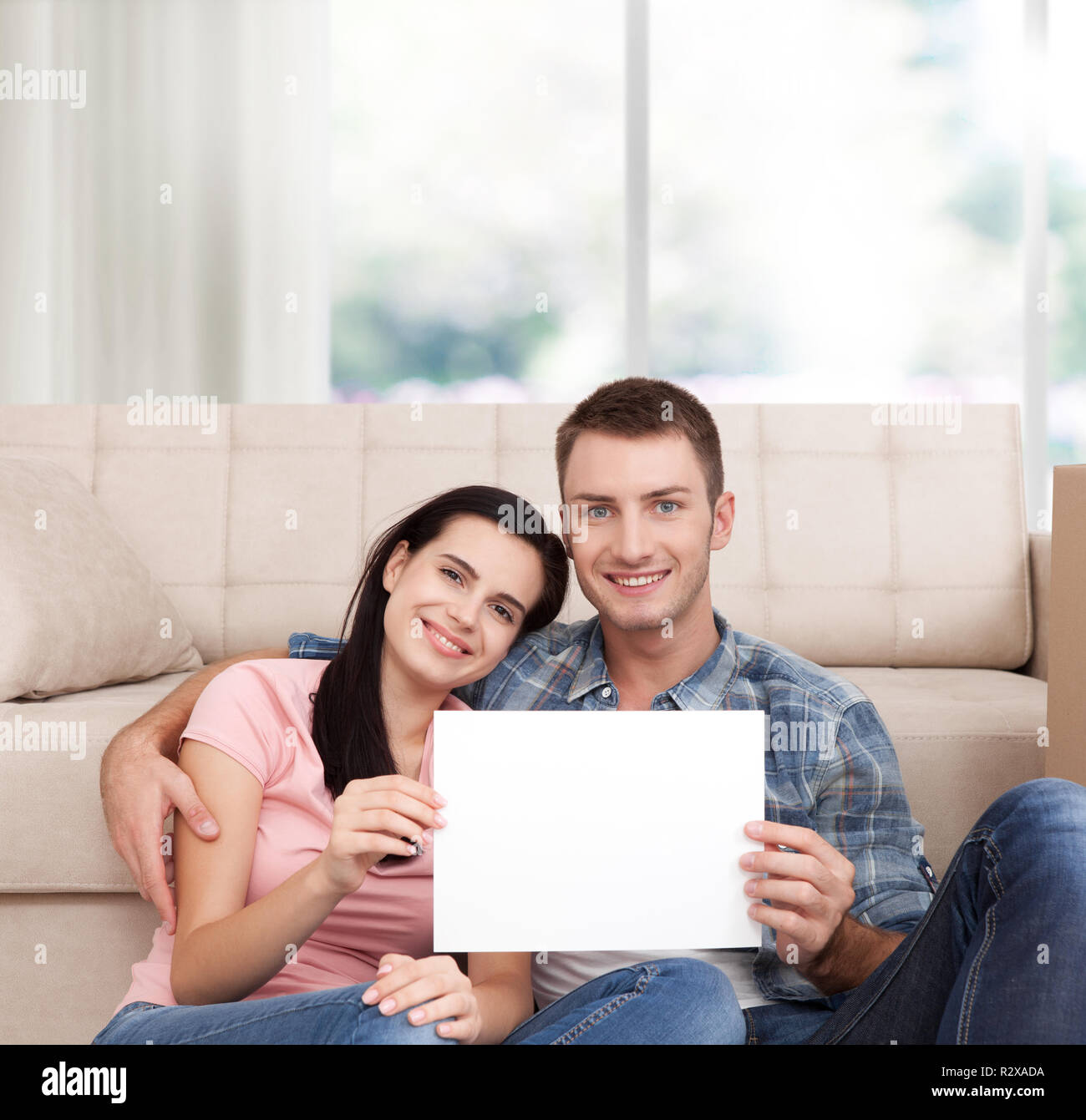 Happy engaged millennial couple in love sitting on couch at home, holding  laptop on lap, sharing computer, using online shopping app, internet  service, talking, chatting, smiling, hugging. Full length Stock Photo