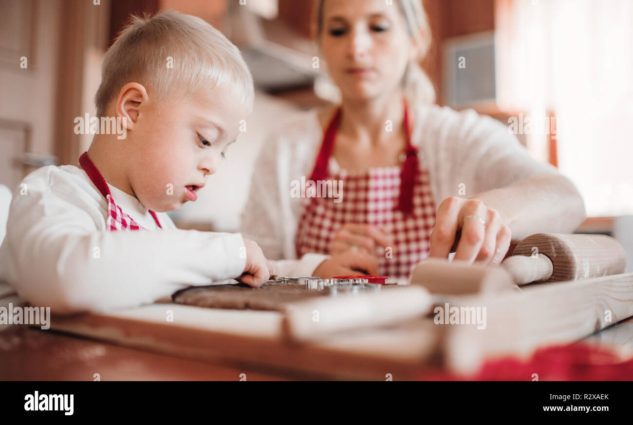 A handicapped down syndrome boy with his mother indoors baking. Stock Photo