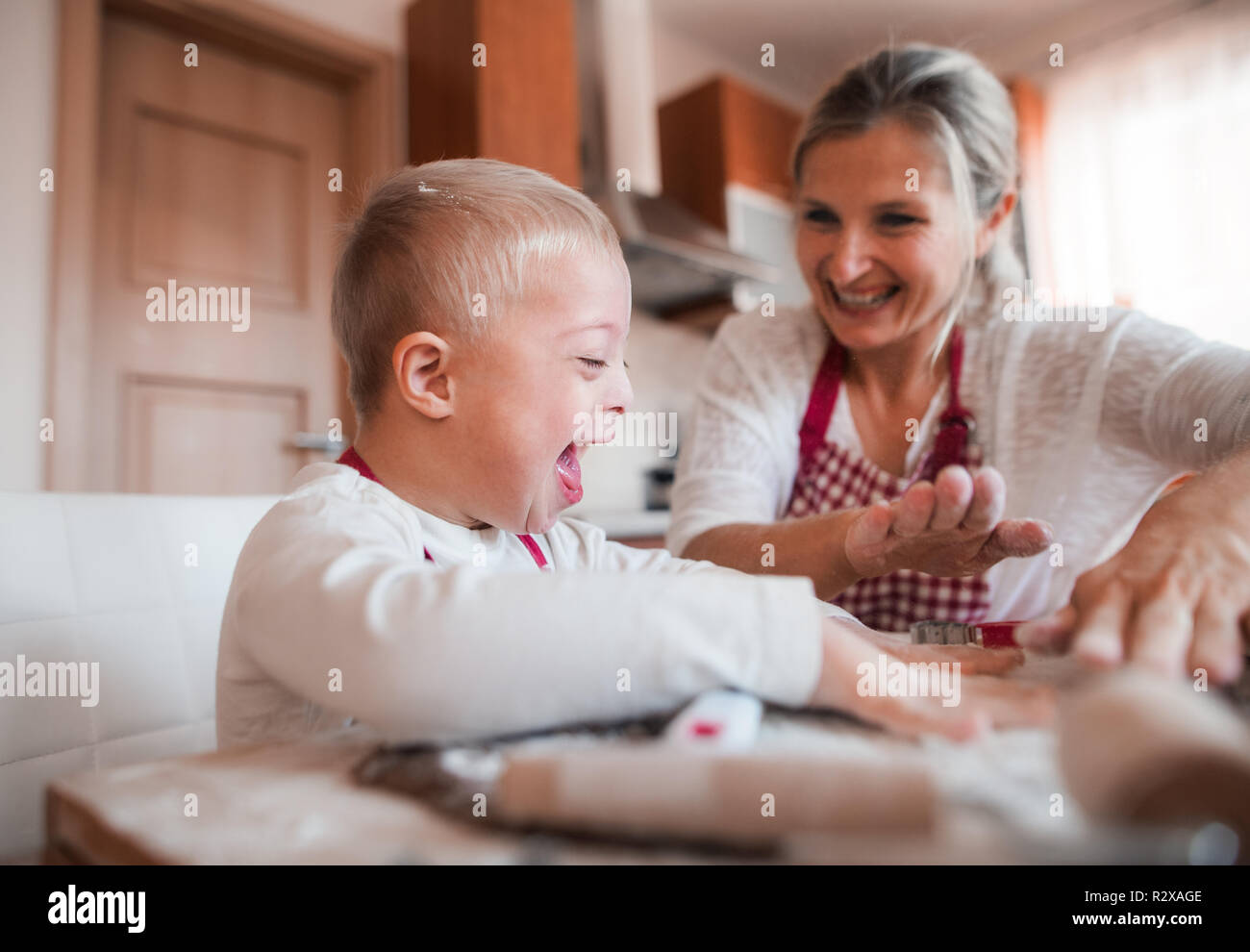 A laughing handicapped down syndrome child with his mother indoors baking. Stock Photo