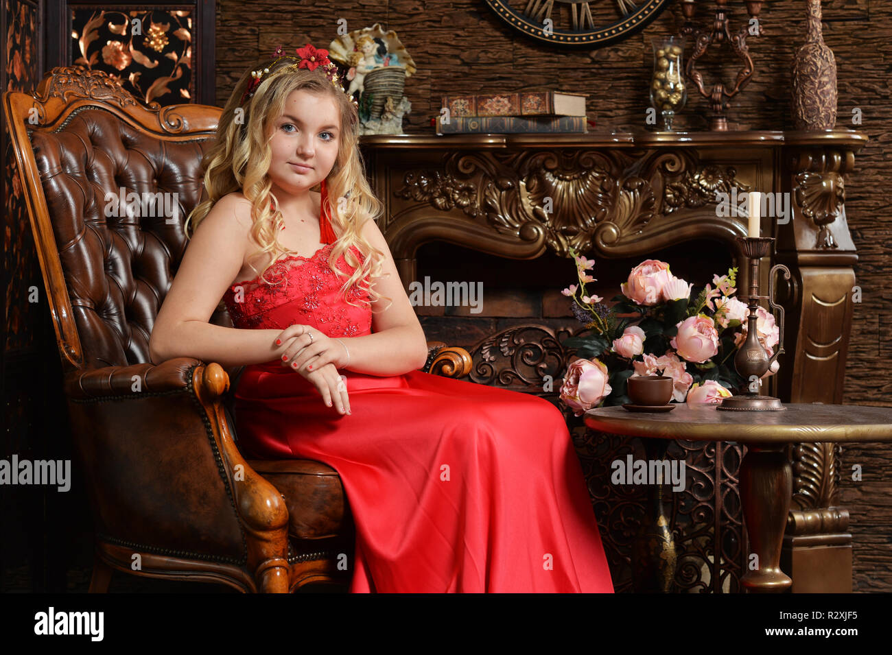 Blonde teenage girl in bright red dress sitting in armchair Stock Photo