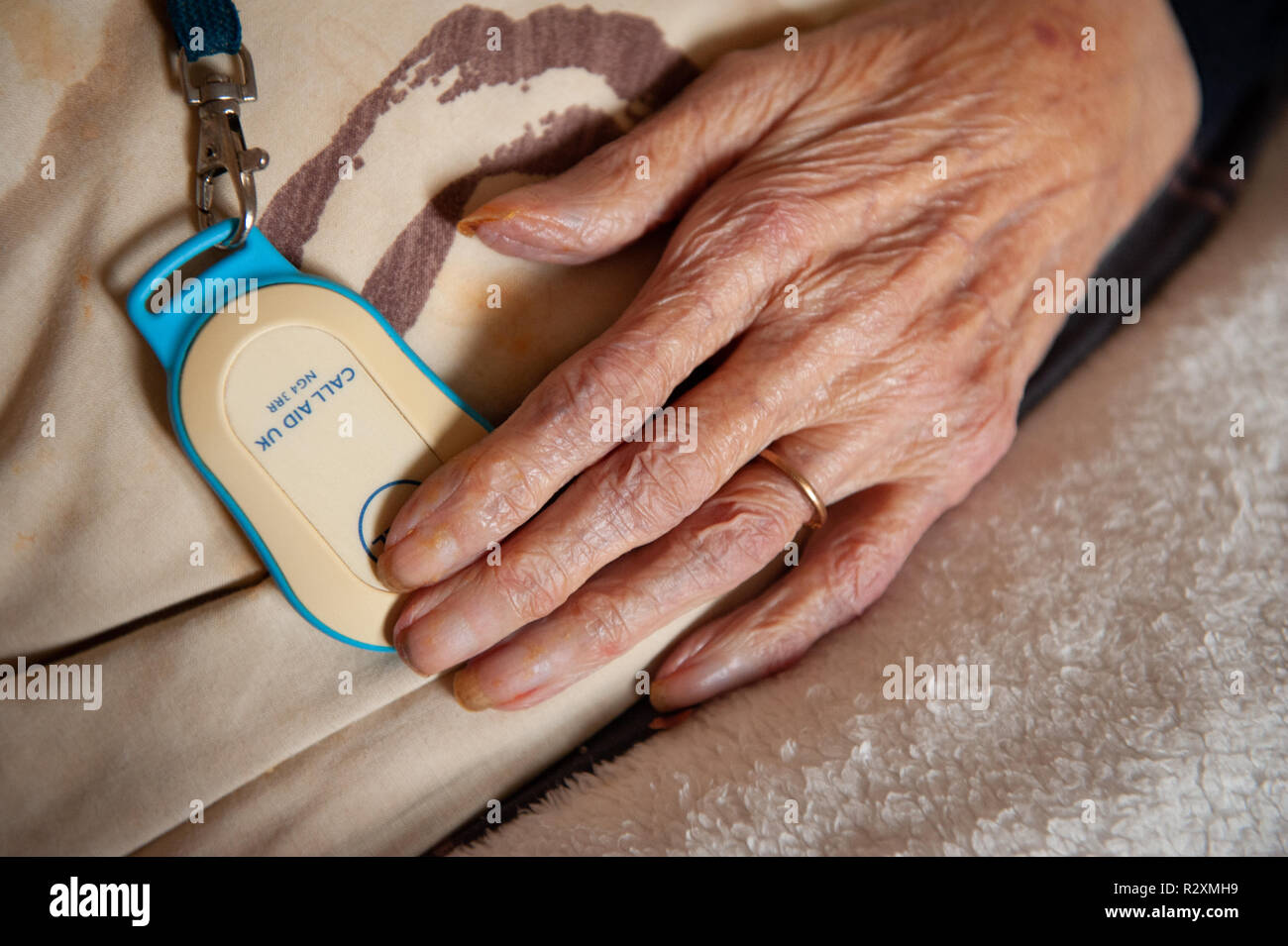 Old lady's hand showing age, call button and gold wedding band. Stock Photo