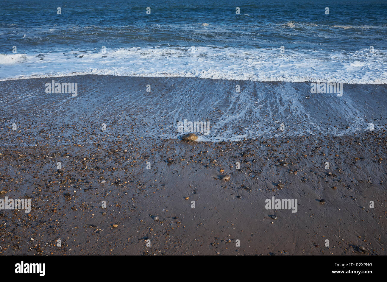 A close up of a beach that has pebbles and stones with the tide going out, England, UK Stock Photo