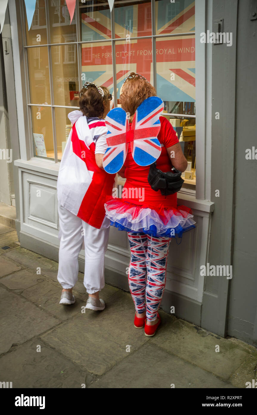 Two women in fancy dress for the Royal Wedding of Prince Harry and Meghan Markle look in a shop window in Windsor, Berkshire Stock Photo