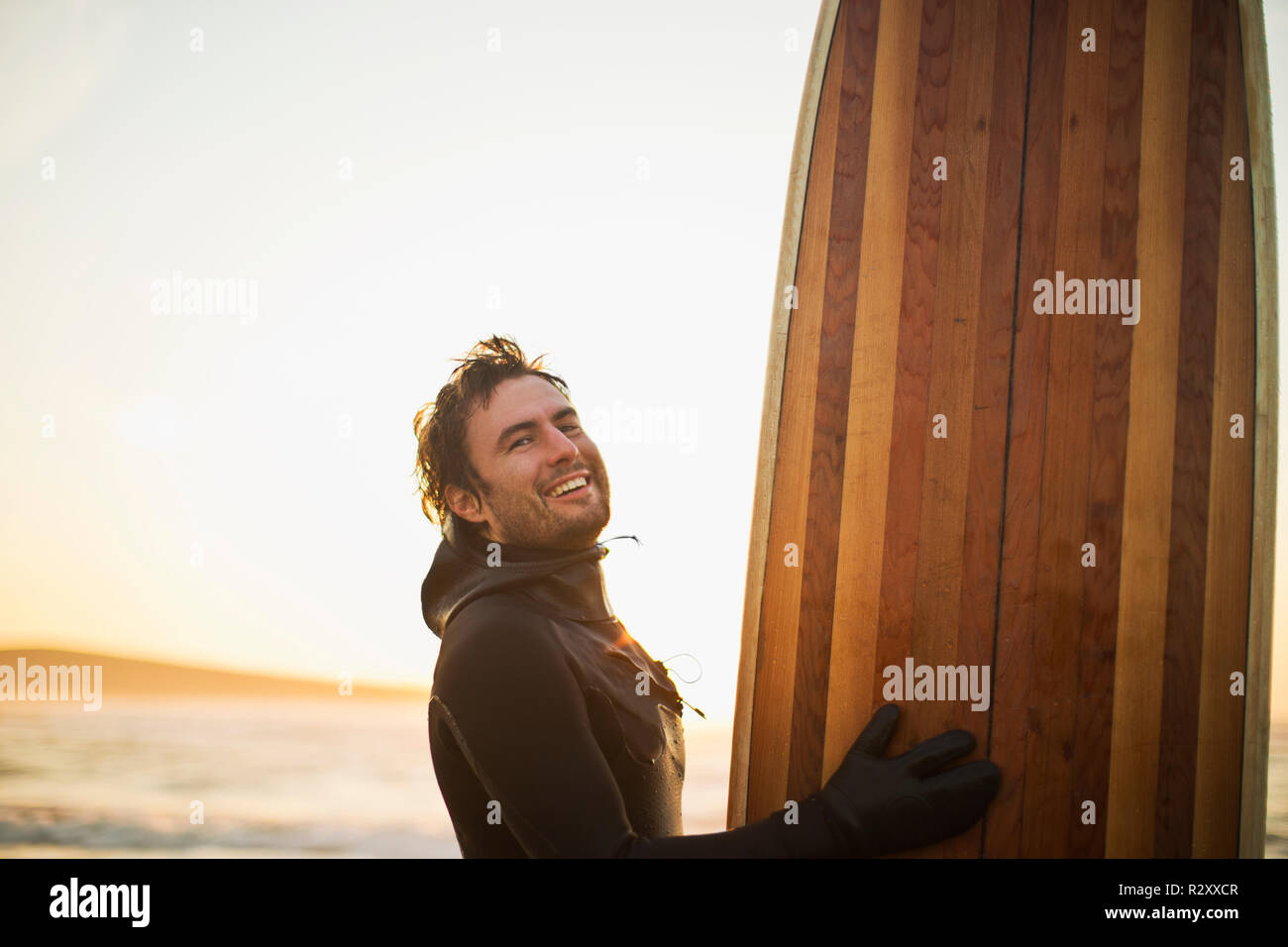 Smiling mid adult man carrying a surfboard on a beach. Stock Photo