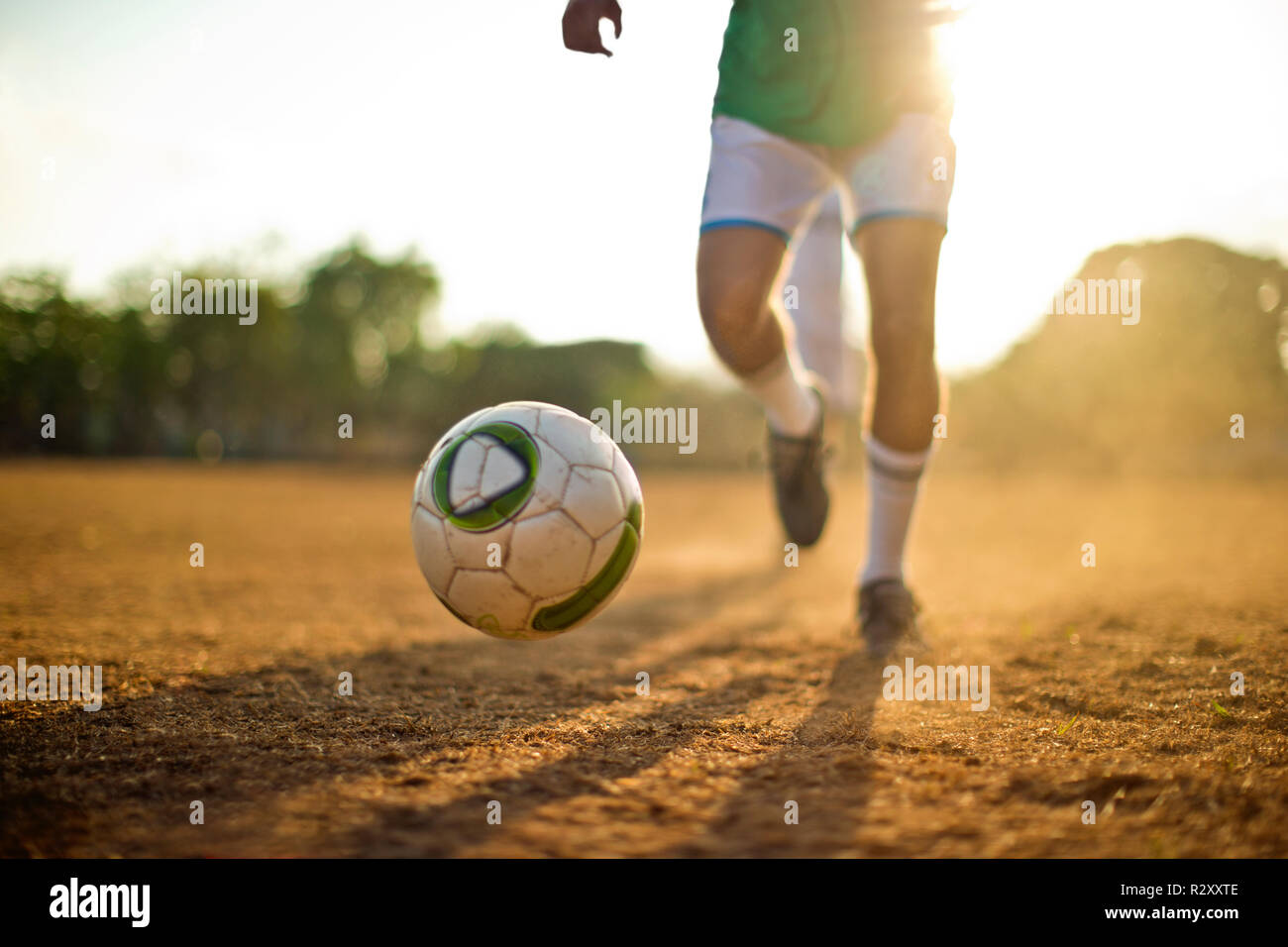 Soccer player chasing a bouncing soccer ball while playing on a dusty sports field. Stock Photo