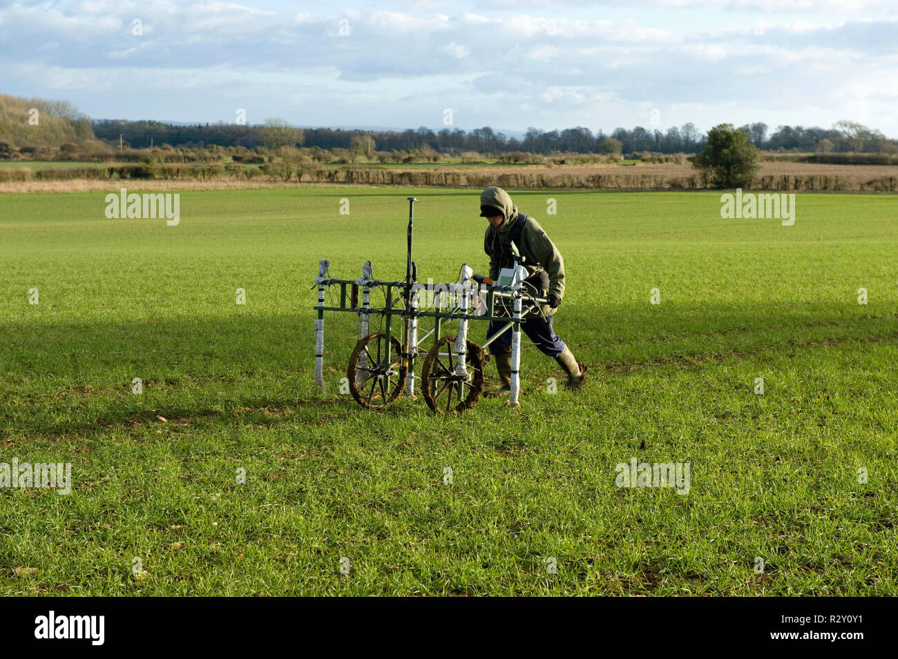 A geophysicist pushing a trolley with ground mapping sensors, creating a geophysical survey of the subsoil in a field. Stock Photo