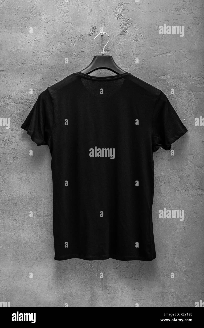 Back side of male black cotton t-shirt on a hanger and a concrete wall in the background. T-shirt without print Stock Photo