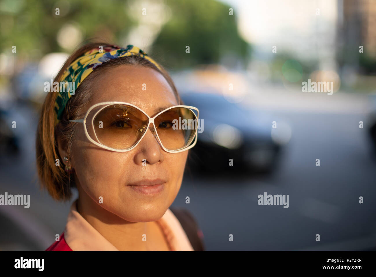 Portrait of confident mature Taiwanese woman of Chinese ethnicity in evening sun against big city traffic backdrop Stock Photo