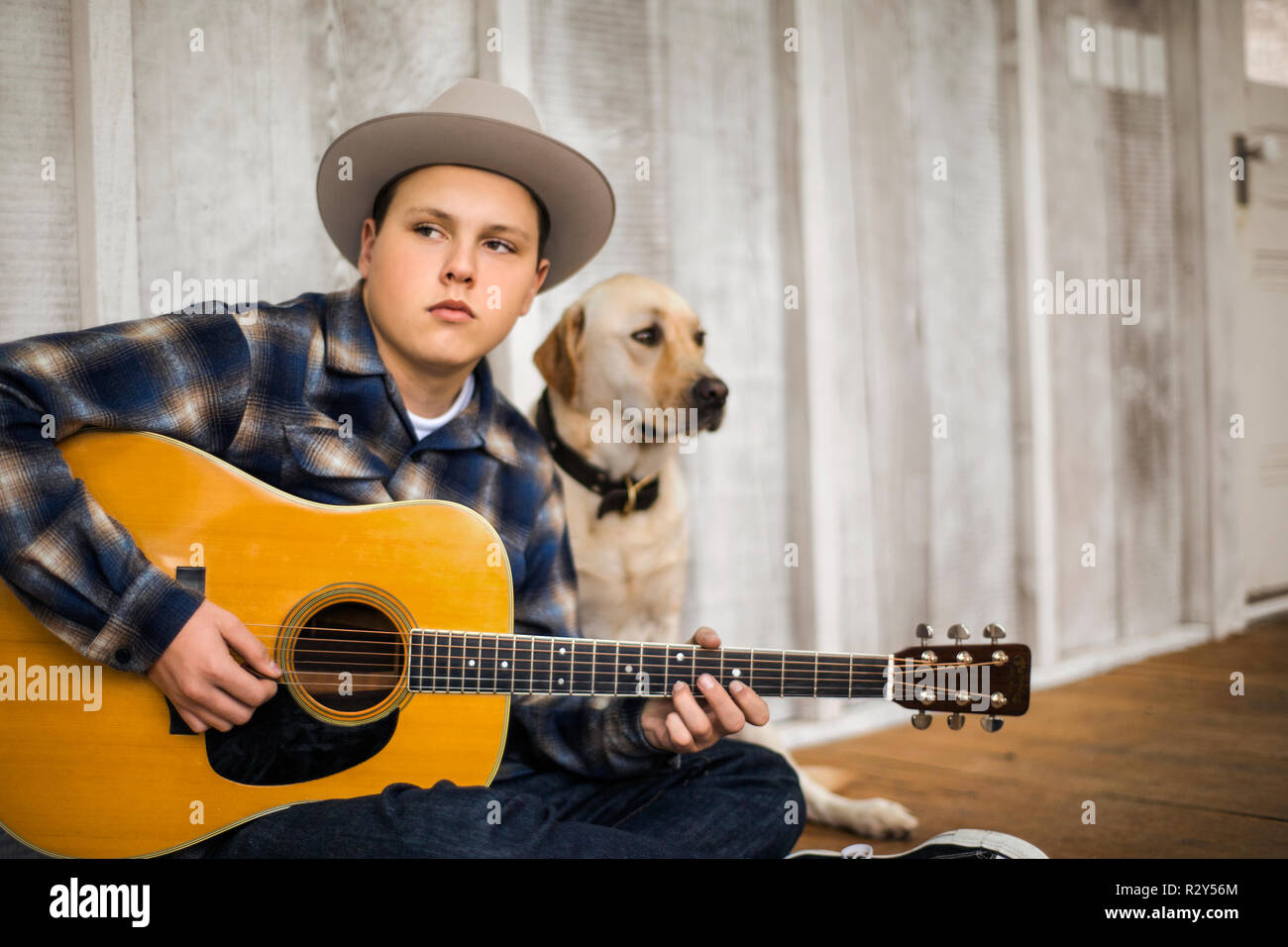Teenage boy playing an acoustic guitar with his dog. Stock Photo