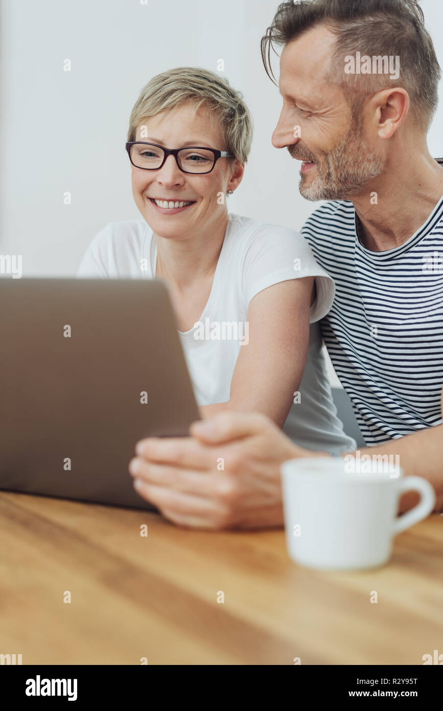 Woman beaming happily as she browses the internet on a laptop computer watched by her affectionate husband alongside her Stock Photo