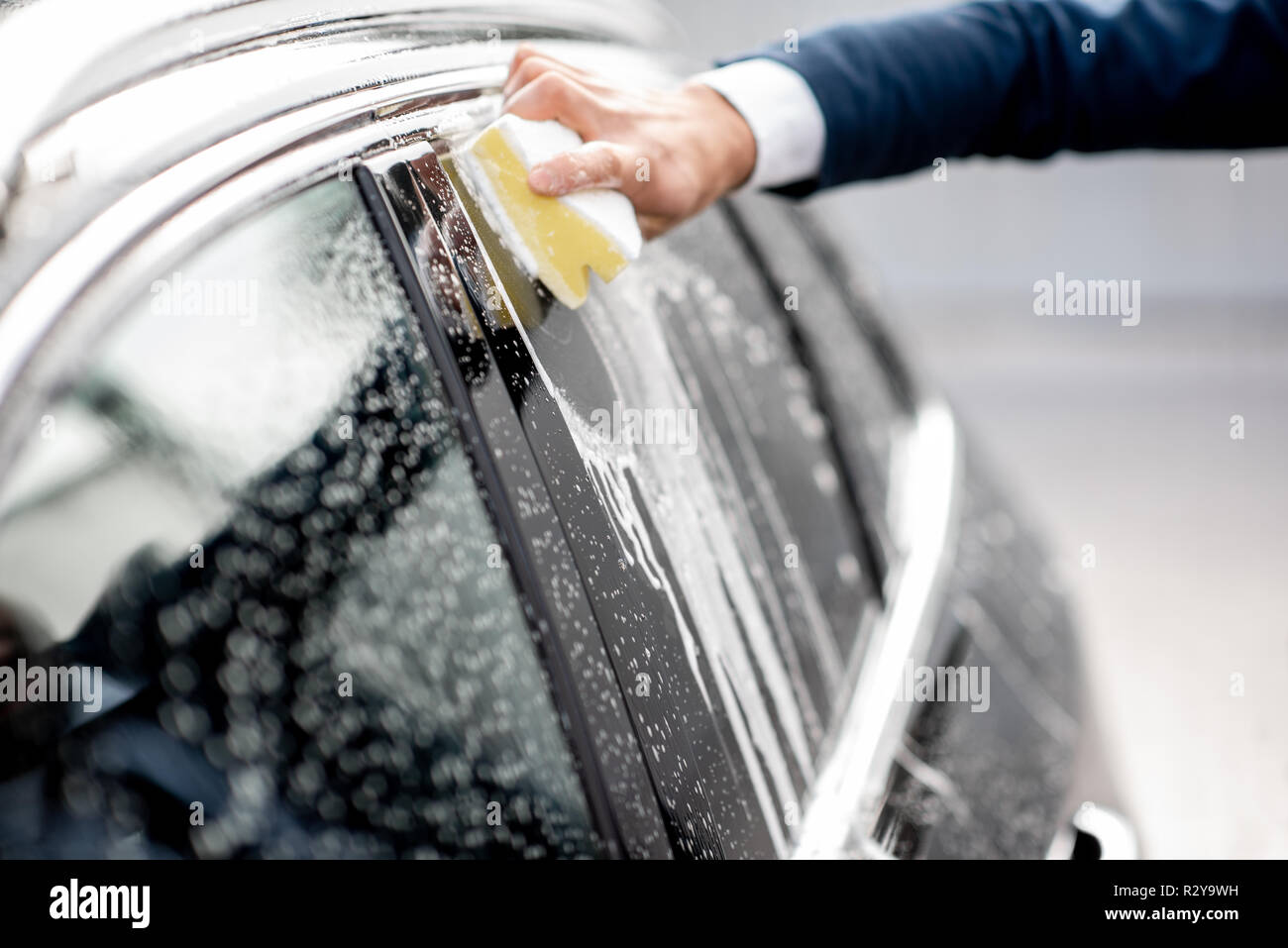 Businessman washing car window with sponge and foam on a self service