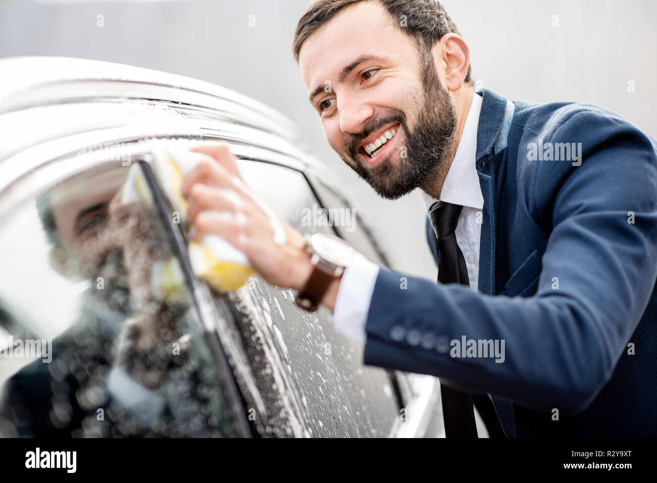 Elegant businessman dressed in the suit washing his car with yellow sponge on a self service open air car wash Stock Photo