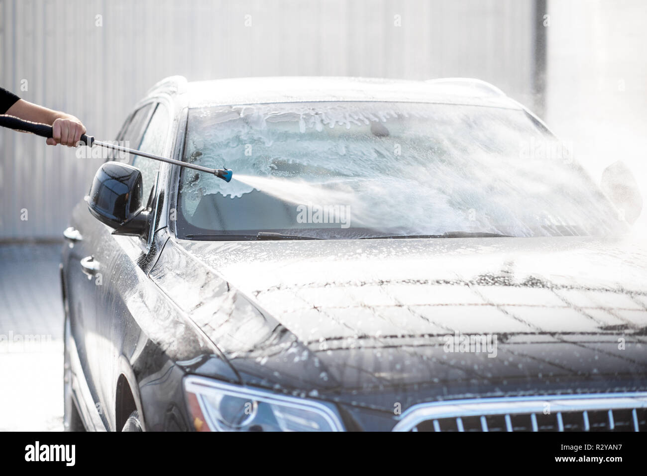 Professional washer in black uniform washing luxury car with water gun