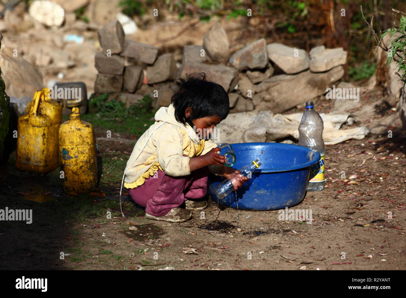 Indigenous child playing with plastic bottle and water in Andean village, Bolivia Stock Photo