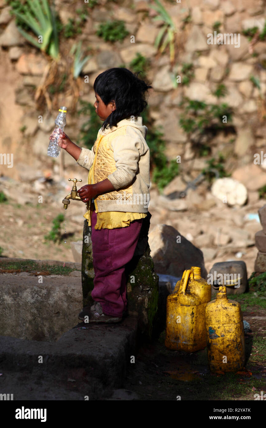 Indigenous child holding empty plastic bottle next to water tap in Andean village, Bolivia Stock Photo