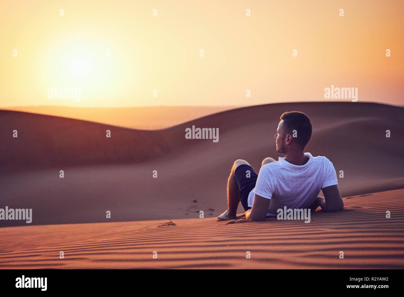 Idyllic sunrise in desert. Young man contemplation on sand dune. Wahiba Sands in Oman. Stock Photo