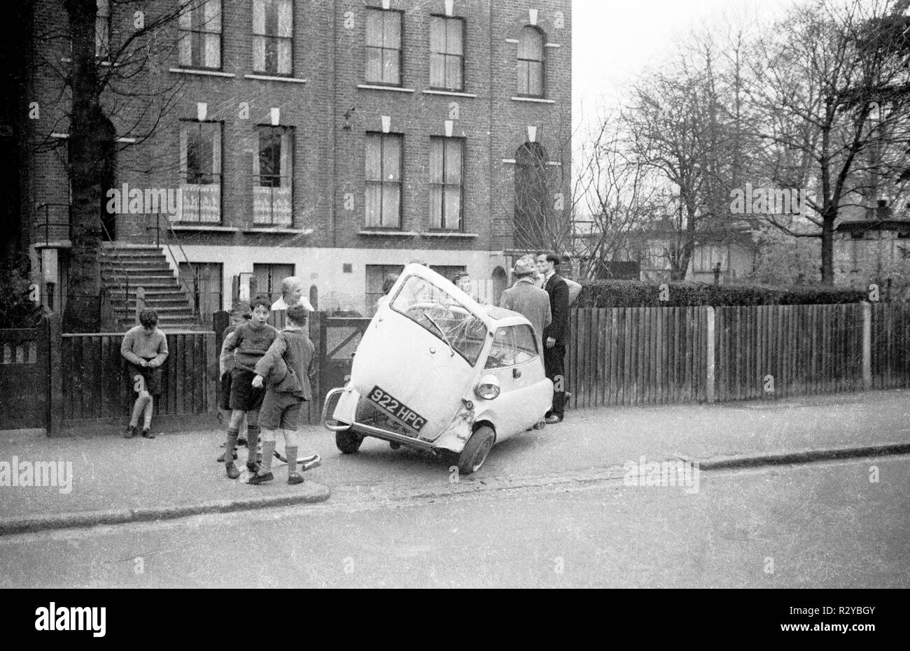 BMW Isetta bubble car damaged in accident in 1959 with onlookers and an estate of prefabs in background built where a flying bomb landed in WW2. Lee Green SE3. There is a colourised version R2YBK5. Stock Photo
