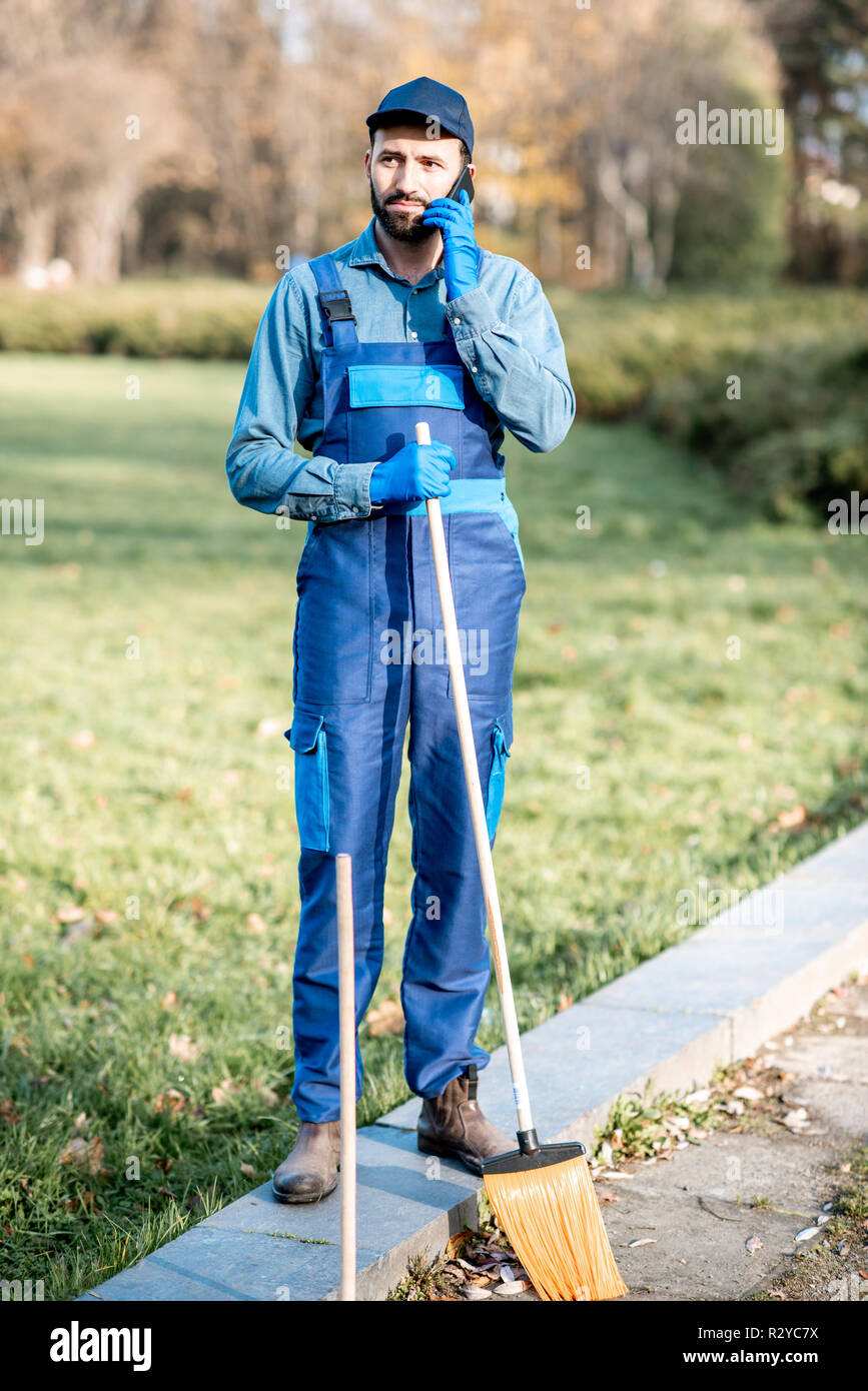 Portrait of a male sweeper in uniform with working tools talking with