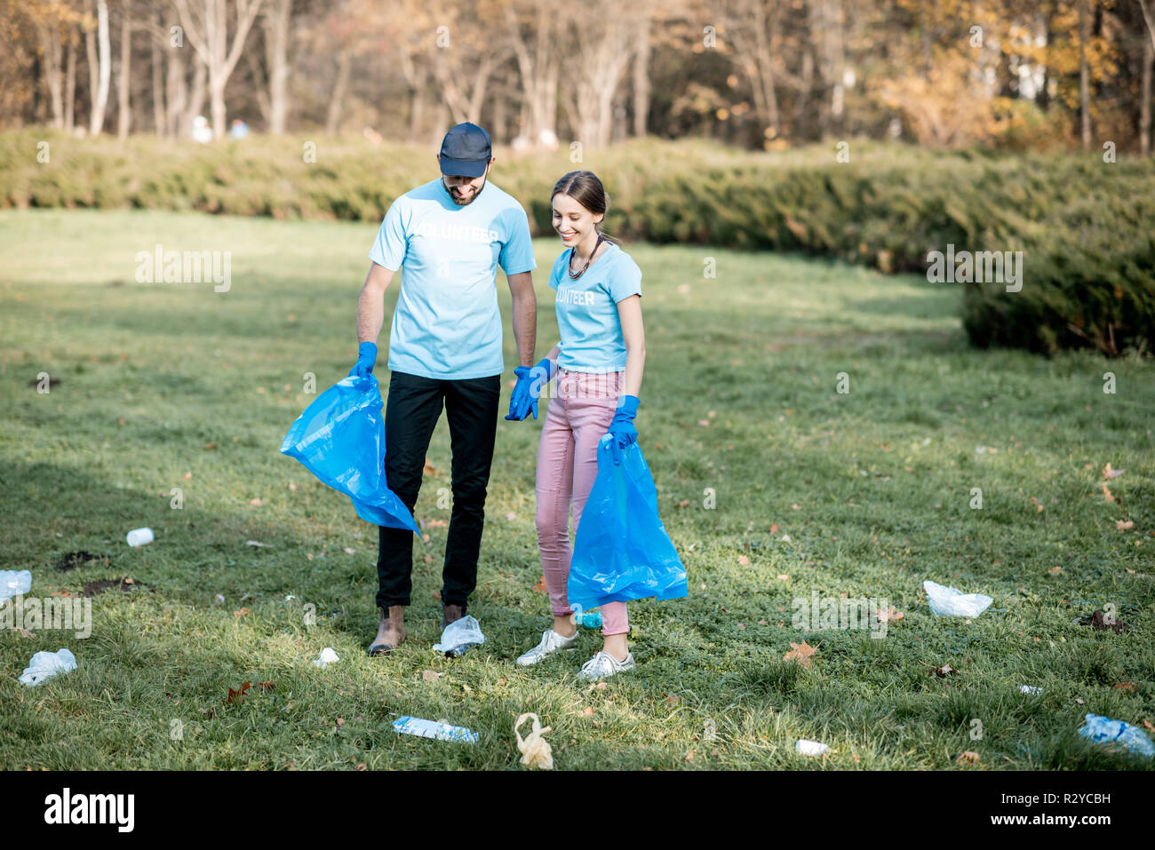 Man and woman volunteers dressed in blue t-shirts cleaning public garden from plastic rubbish into the bags Stock Photo