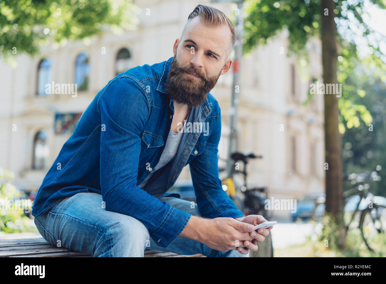 Street Portrait Of Young Bearded Man Wearing Denim Shirt Sitting