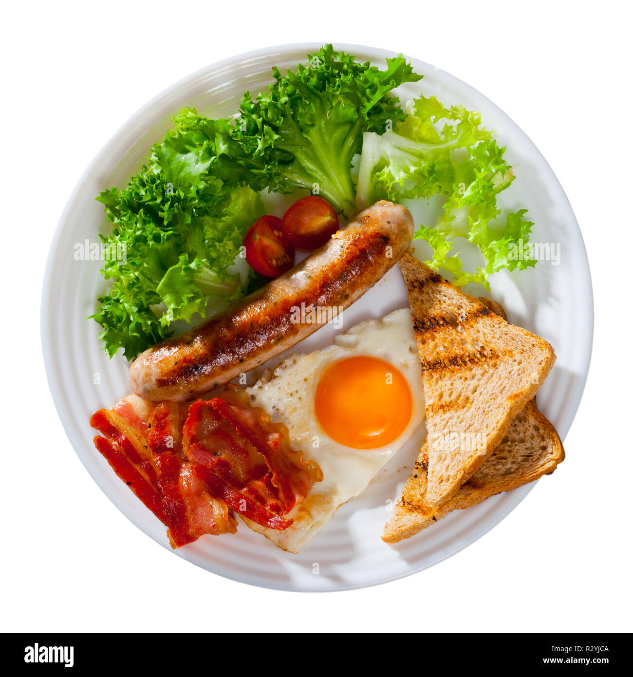Top view of traditional American style breakfast - fried eggs with bacon, sausage and toasts garnished with fresh greens on white plate. Isolated over Stock Photo