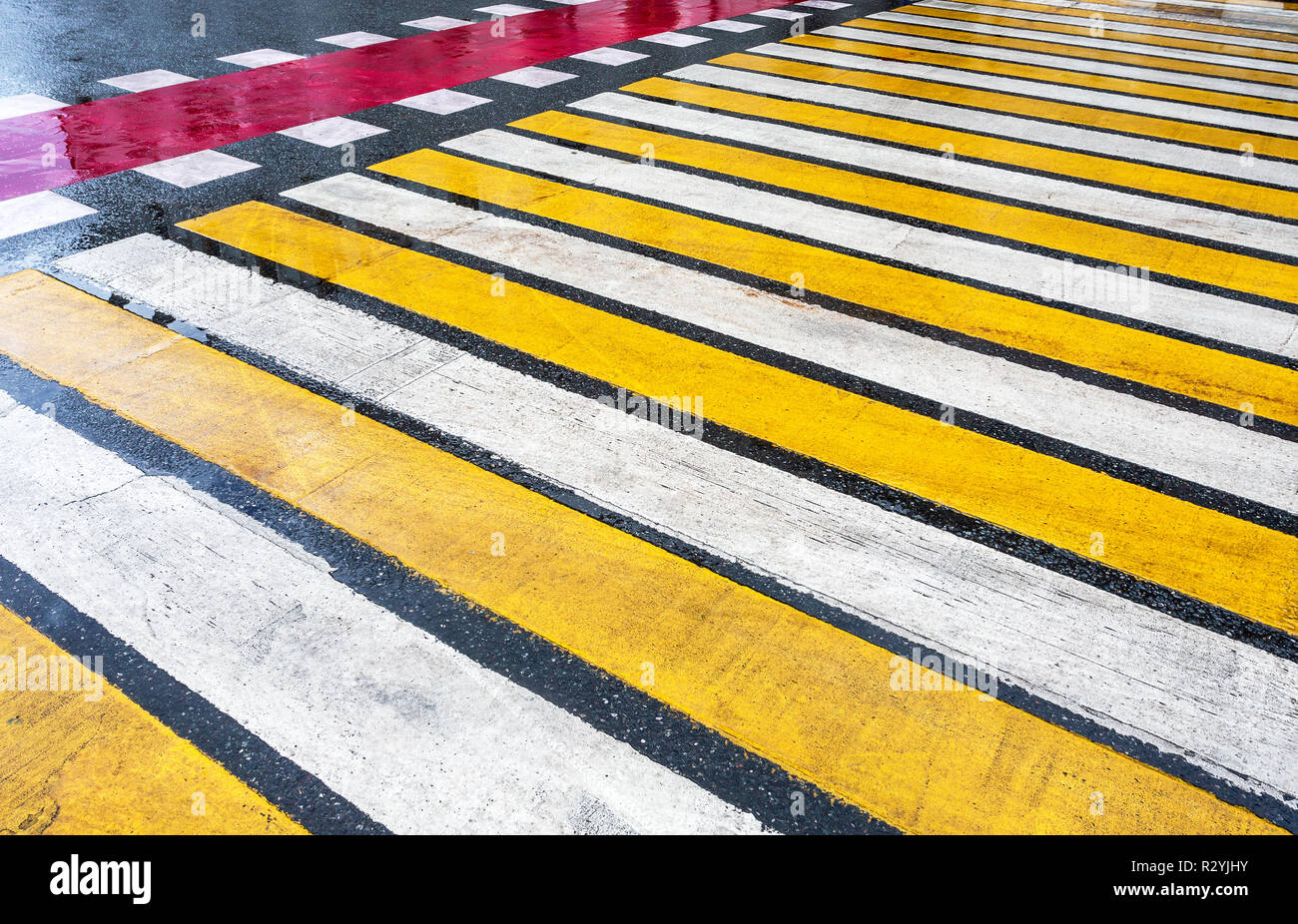 Pedestrian crossing with white, yellow and red stripes on wet asphalt ...