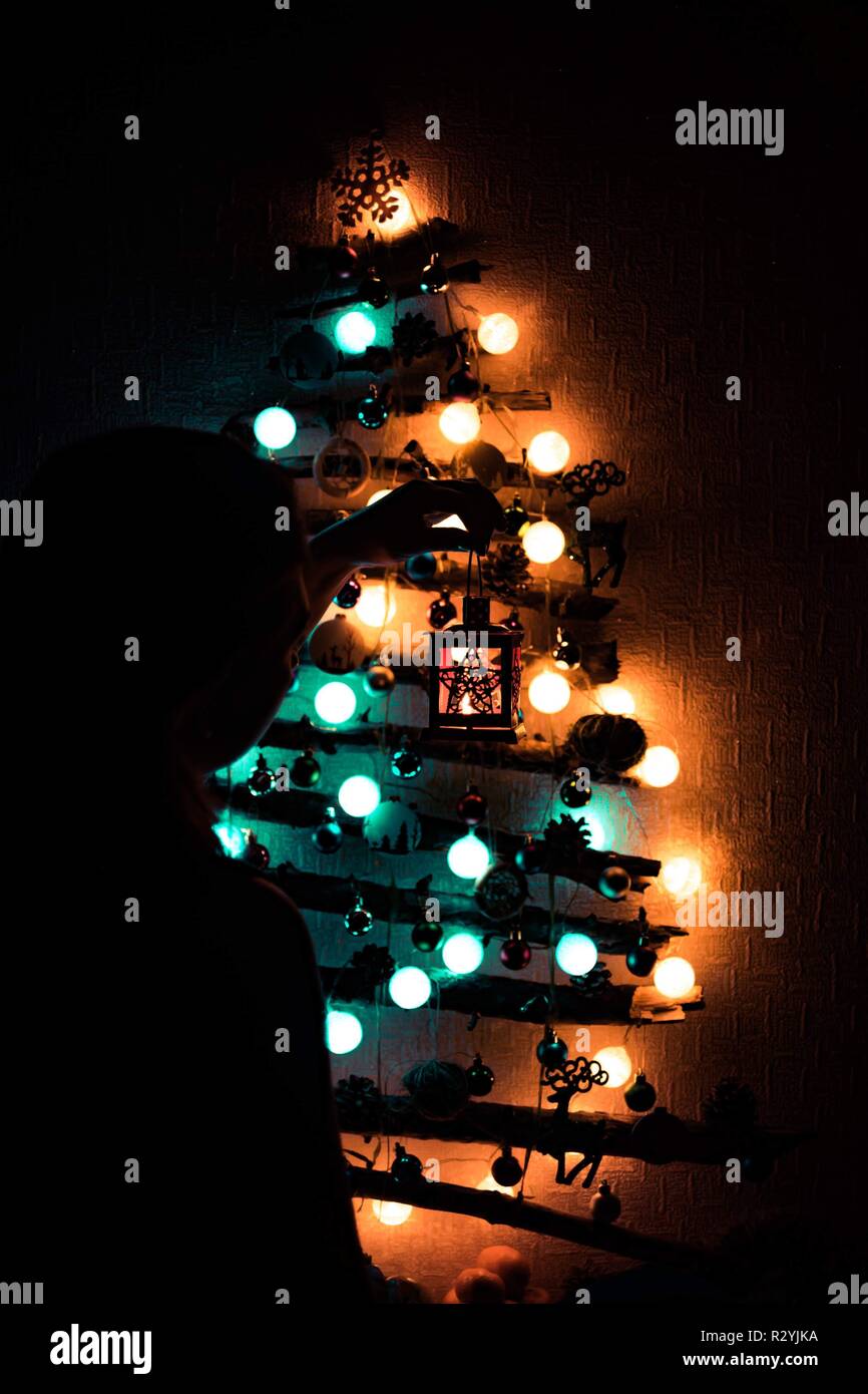The girl decorates a Christmas tree made of sticks hanging on the wall ...