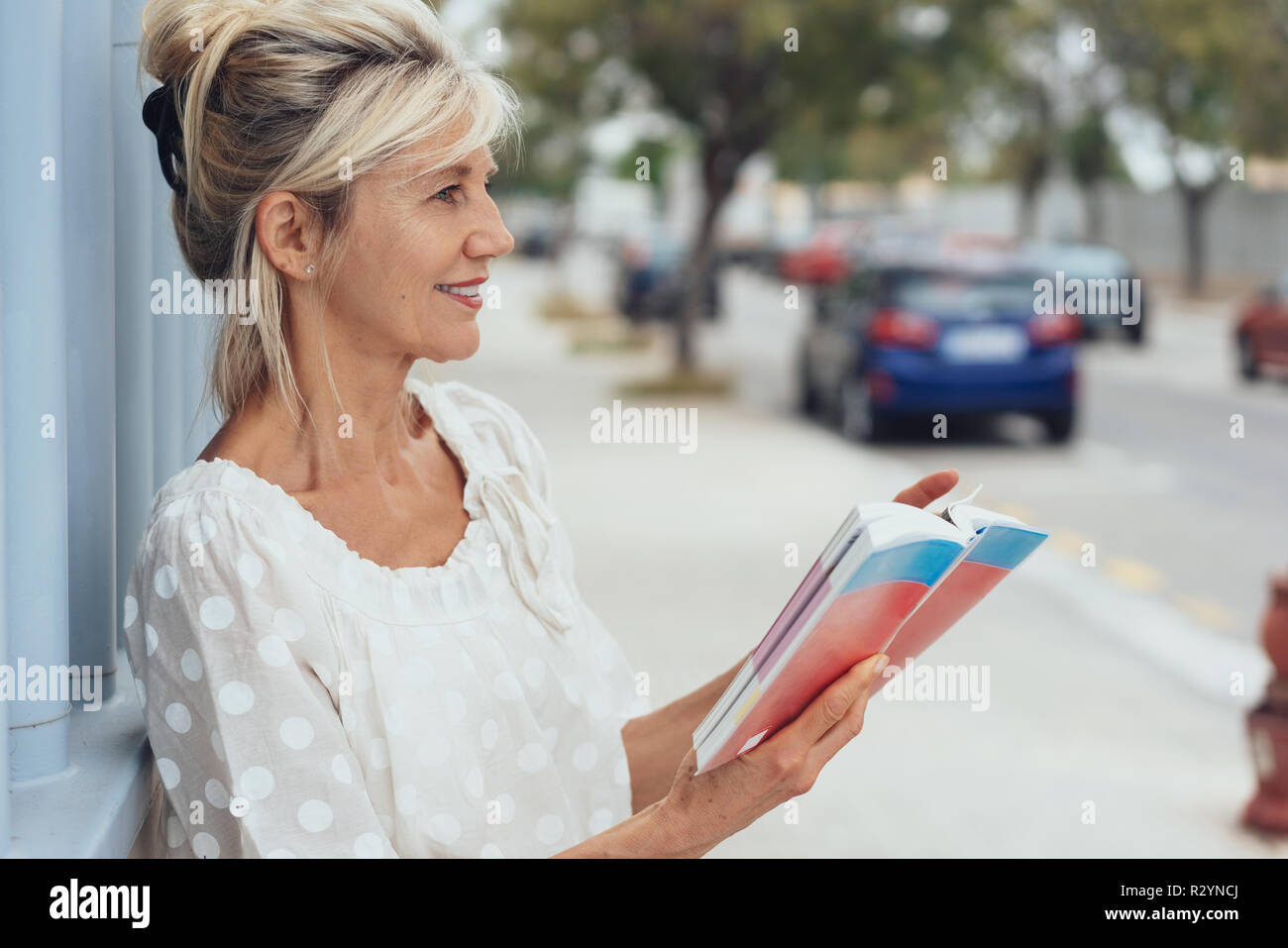 Attractive older woman sightseeing in a city standing in a street with a guide book and tablet in a close up profile view Stock Photo