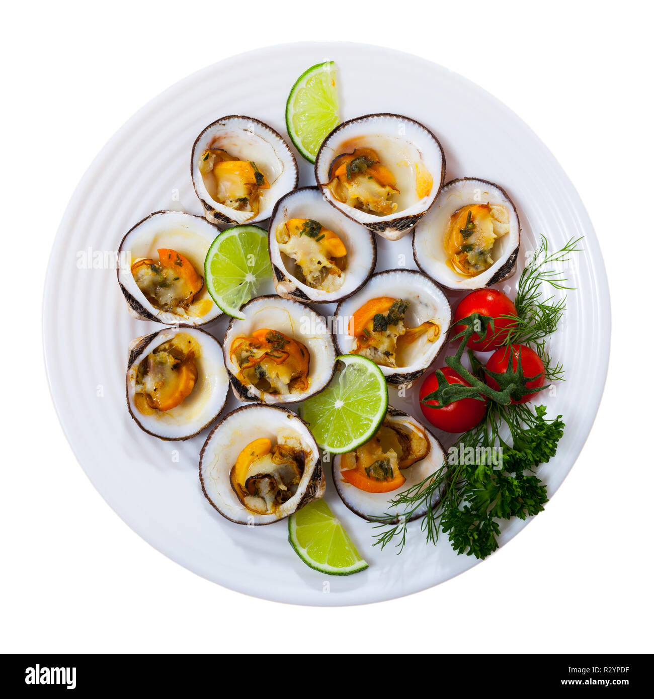 Top view of baked dog cockles served on white plate with lemon, cherry tomatoes and greens. Isolated over white background Stock Photo