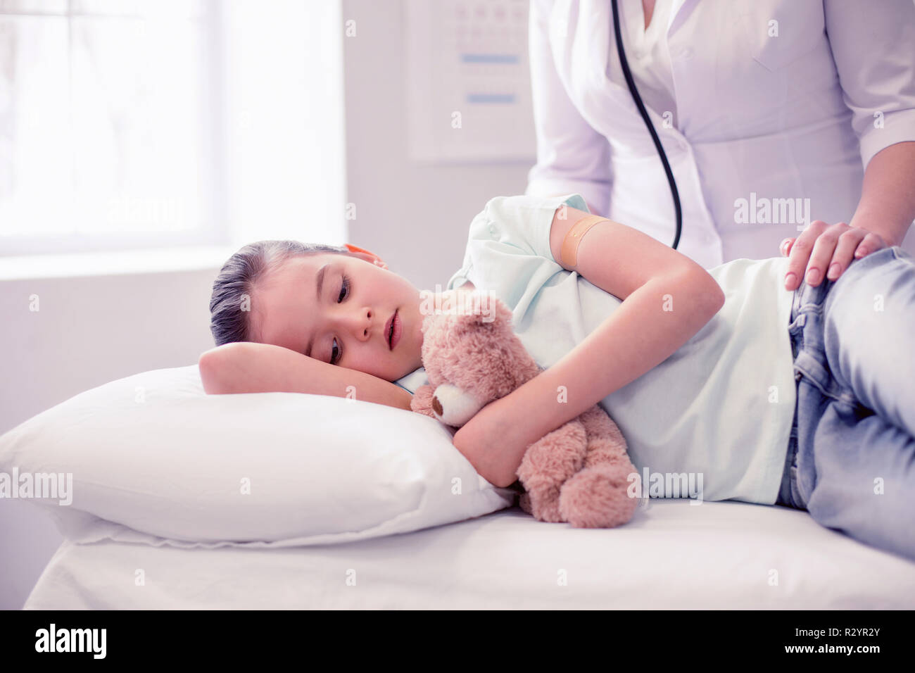 Little cute girl feeling very sick lying on bed in hospital with her toy Stock Photo