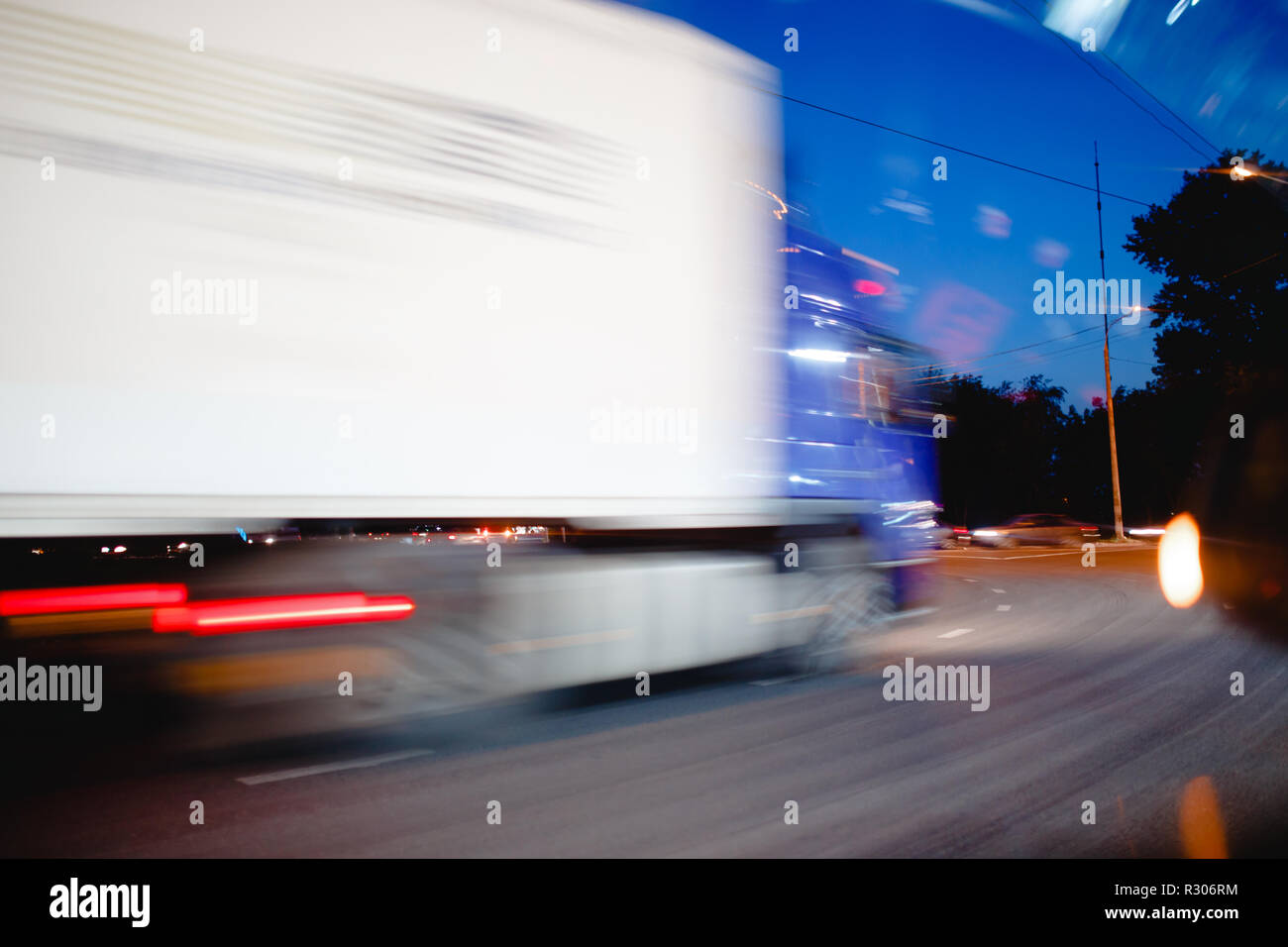 Speeding motion blur trucks with glowing lights on the highway after sunset Stock Photo