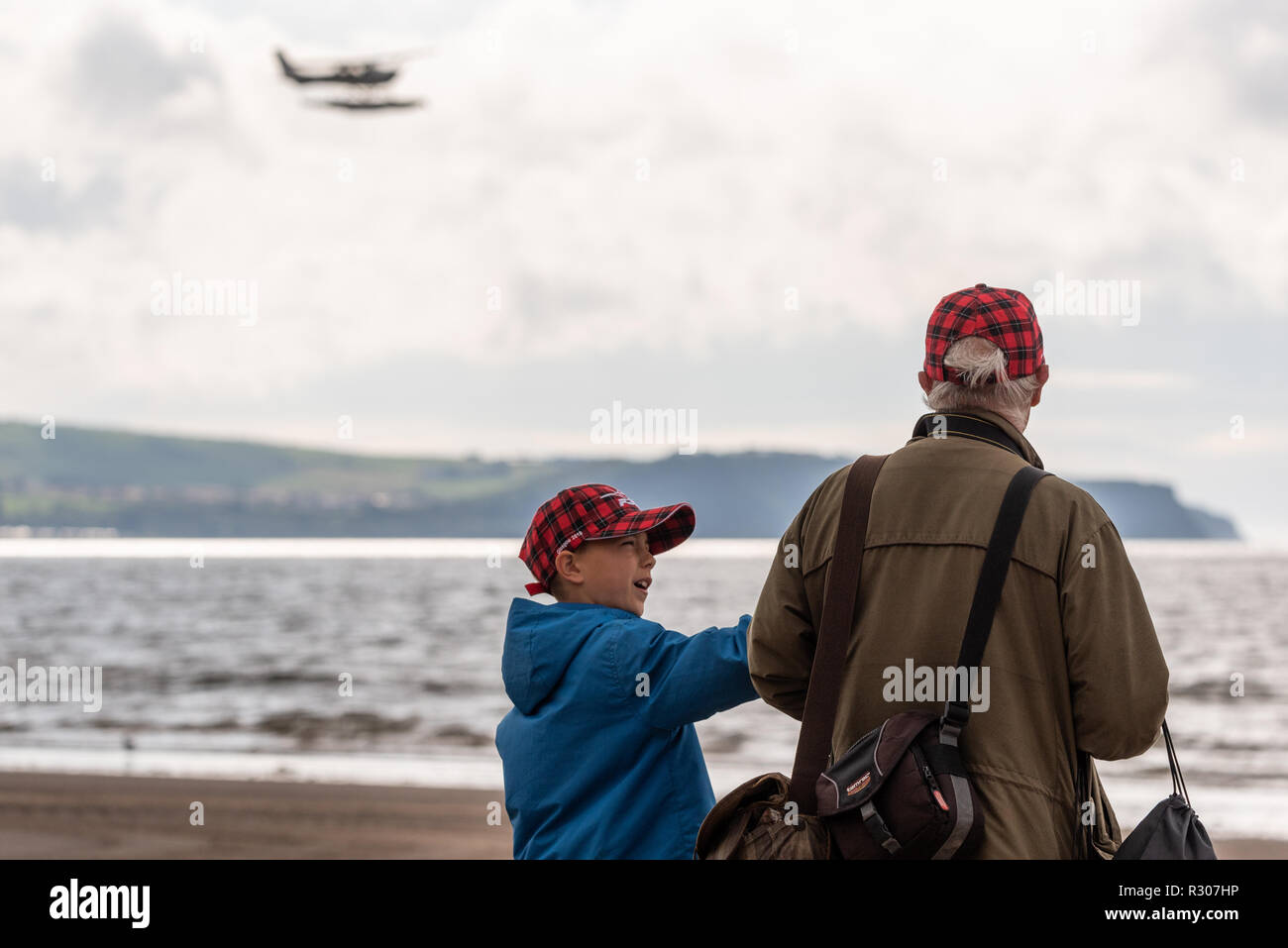 Grandfather and grandson standing on beach at Scottish International Air Show 2018 wearing matching Red Arrows hats Stock Photo