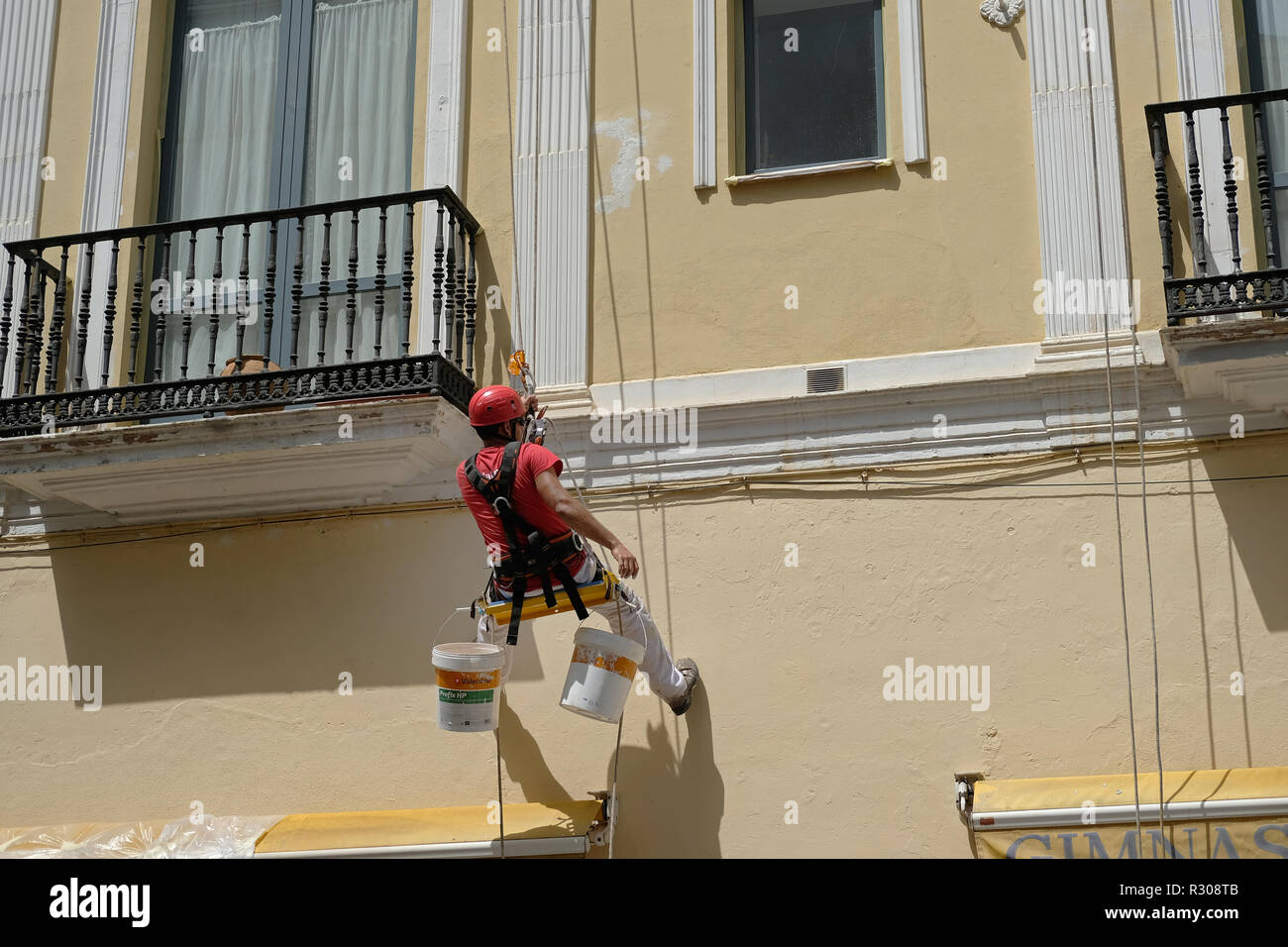 A decorator paints a house whilst hanging from a pulley hoist in Cordoba, Spain. Stock Photo
