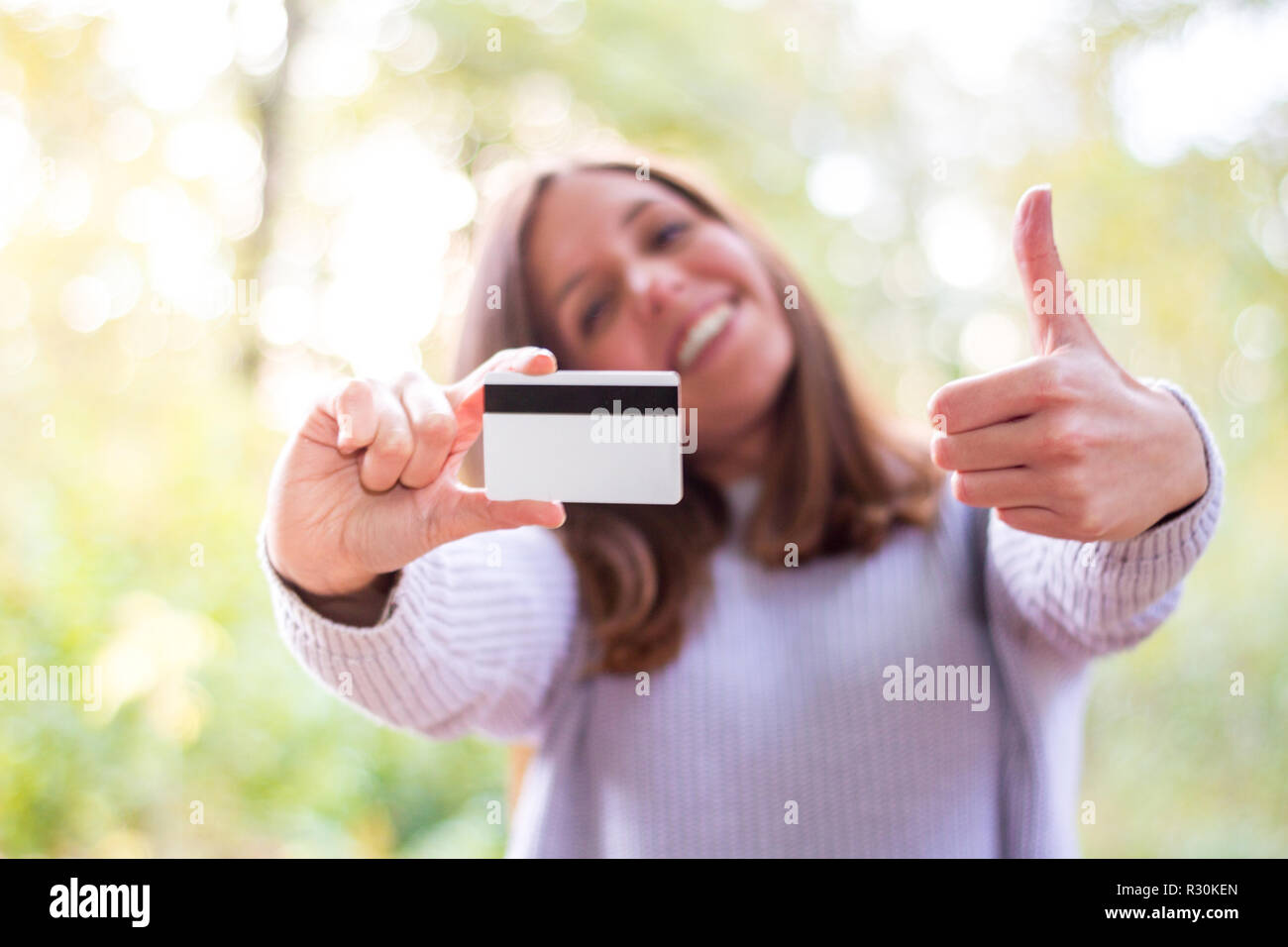 Happy european caucasian young woman or girl holding a credit or debit card and making approval gesture thumbs up because she just made a new card wit Stock Photo
